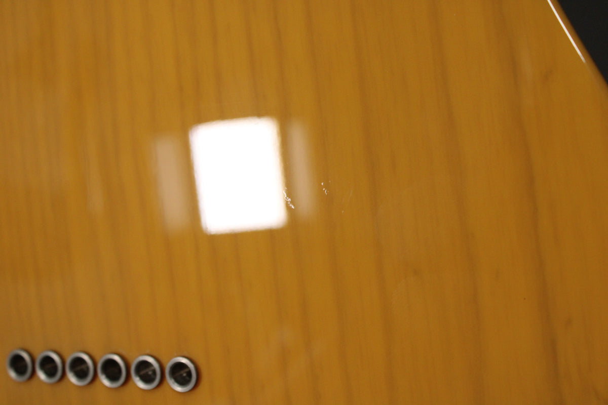 Close-up of the glossy butterscotch blonde body, showing six string ferrules and a few small dings and scratches near a bright reflection.