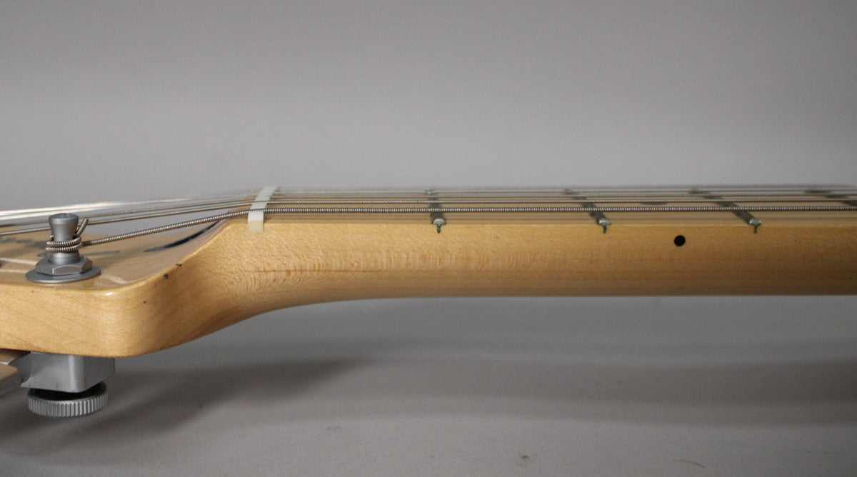 Side view of the maple neck and fretboard, showing a string tree, nut, and dot inlays on the light wood.