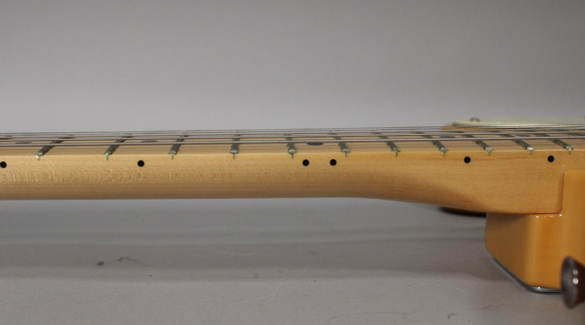 The guitar's light maple neck and fretboard are shown from the side, with black dot inlays and a hint of the butterscotch body.