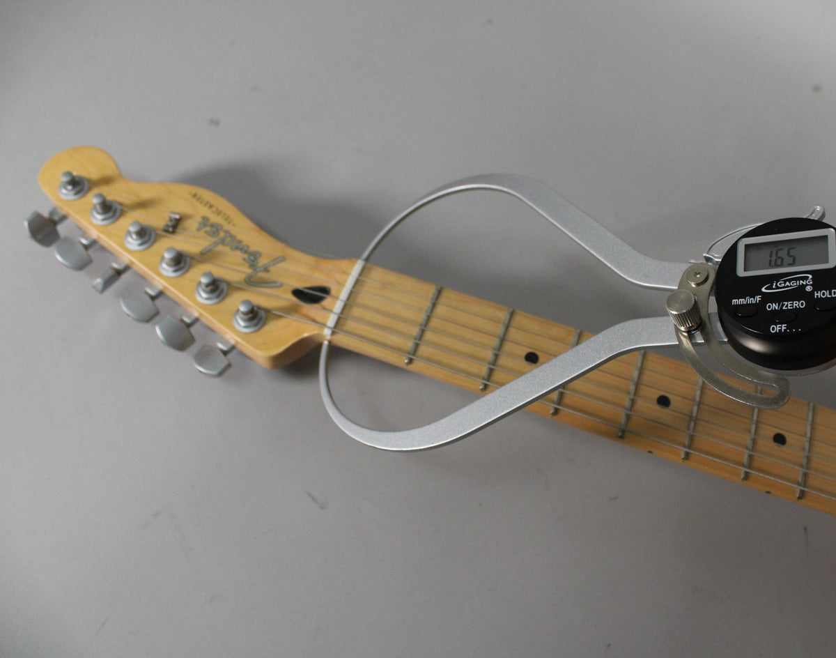 Close-up of the guitar's headstock and maple fretboard, with a digital caliper measuring the nut width at 1.65 inches.