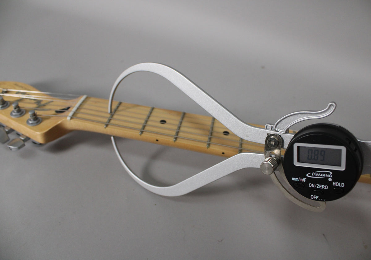 The guitar's maple neck and headstock are measured by a digital caliper showing 0.89, with visible fret wear.