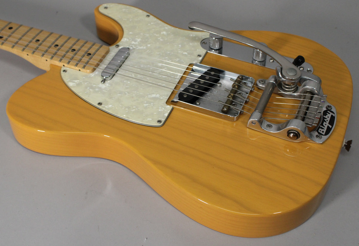 The butterscotch blonde Telecaster body, with visible wood grain, features a pearloid pickguard and a chrome Bigsby vibrato.