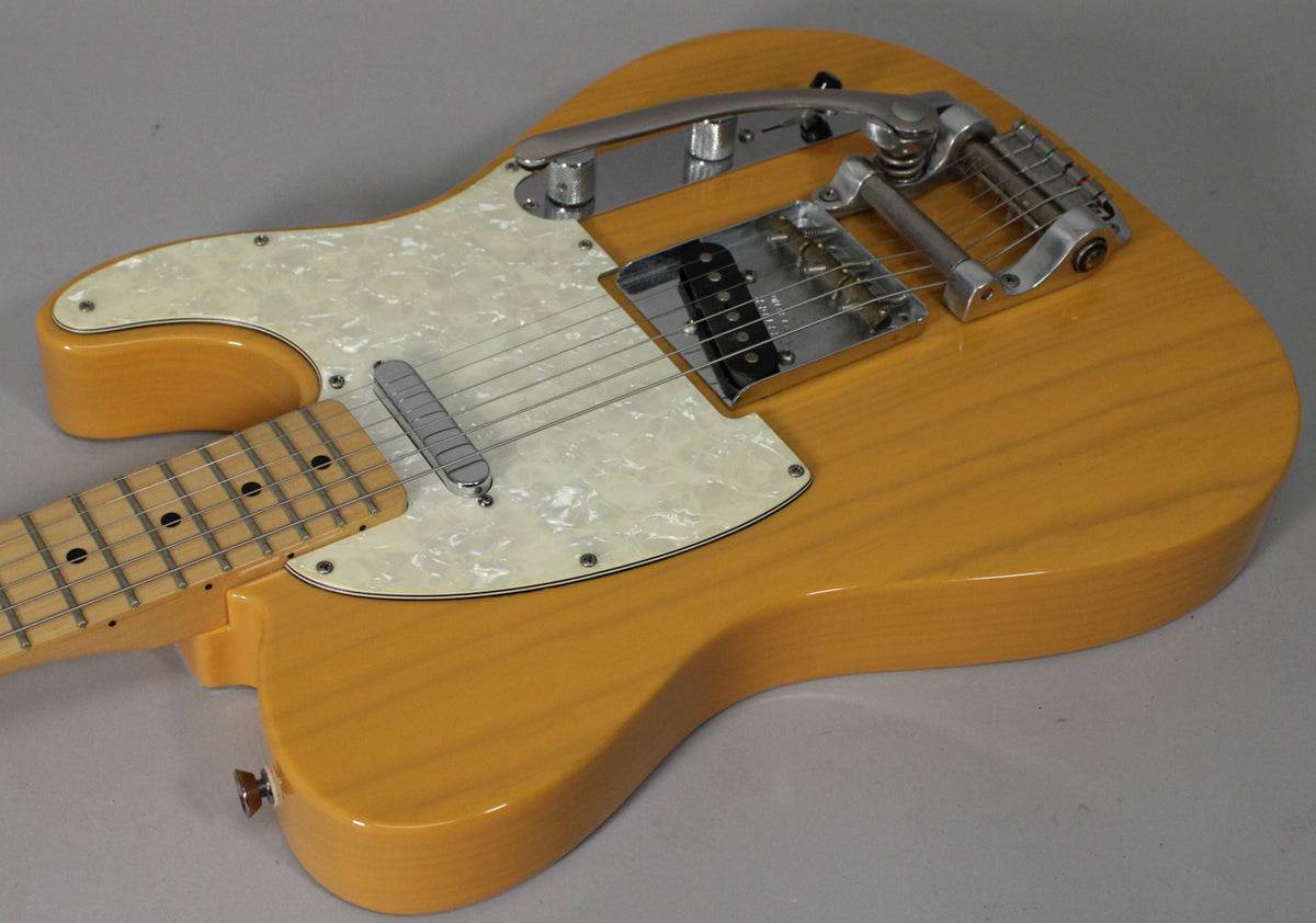 Upper body of a butterscotch blonde Telecaster with a pearloid pickguard, chrome Bigsby tremolo, and a maple fretboard.