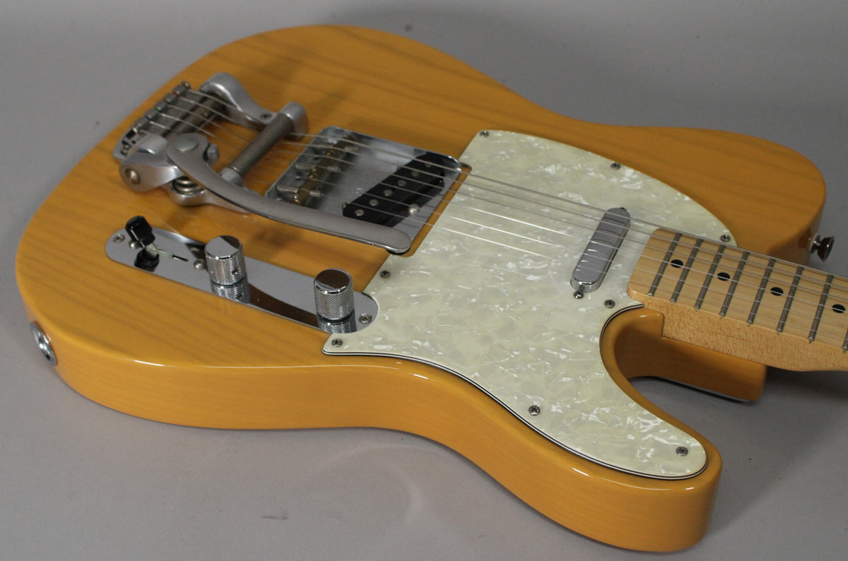 The butterscotch blonde Telecaster body is angled, showing its pearloid pickguard, chrome control plate, and Bigsby vibrato.