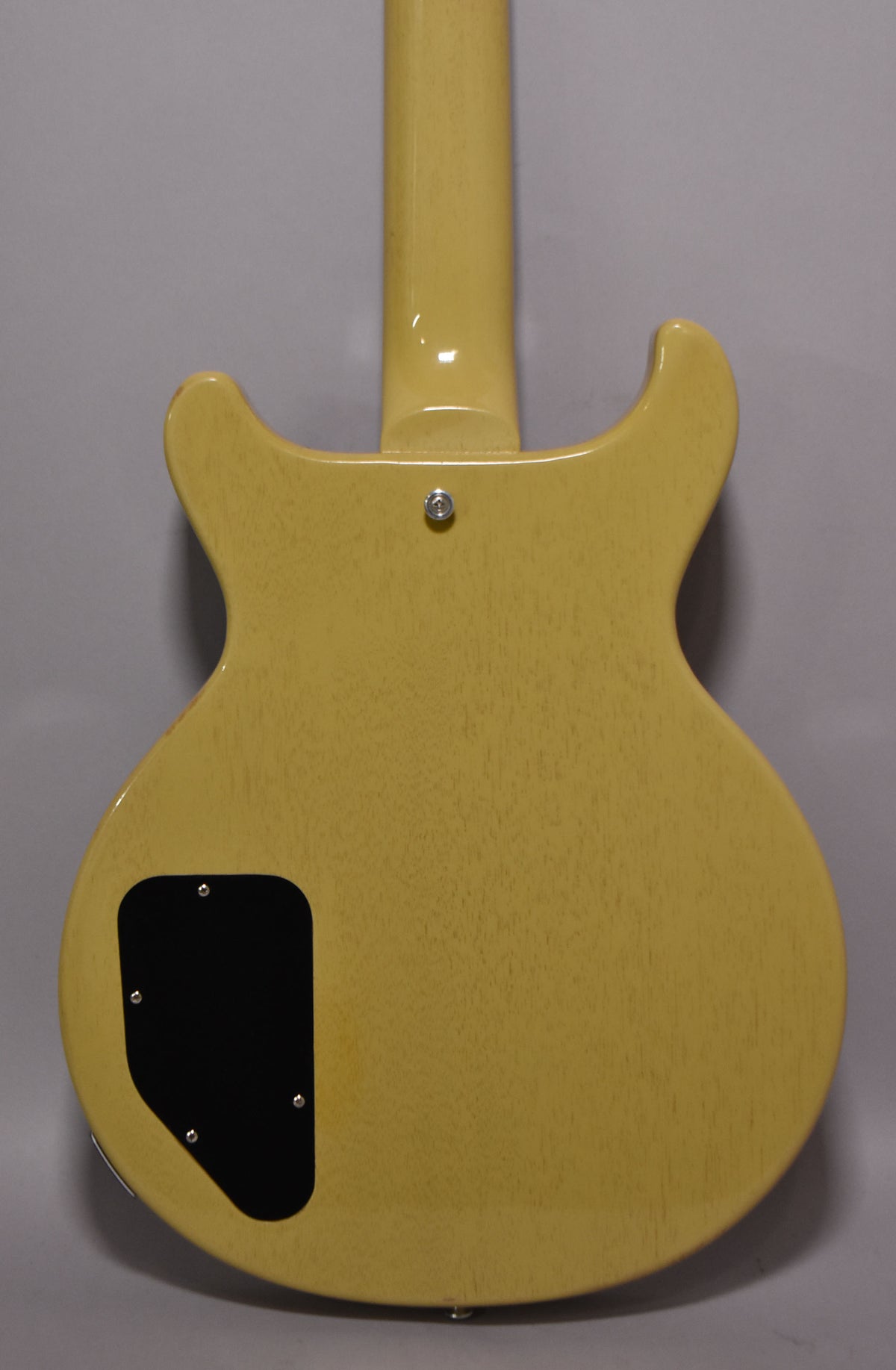 The back of a TV yellow double-cut guitar, showing a black control cavity cover and a chrome strap button near the neck joint.