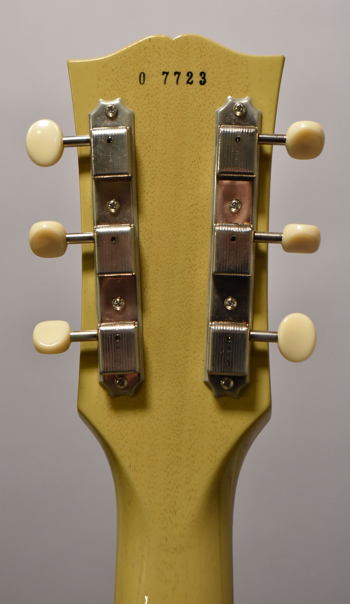 The back of a TV yellow headstock with a serial number "0 7723" and six cream-button tuners, showing light checking.