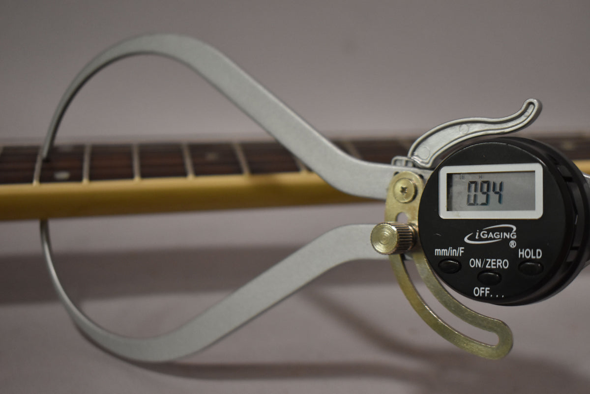 A digital caliper measures the neck thickness at the first fret, showing 0.94 inches, with a dark rosewood fretboard visible.