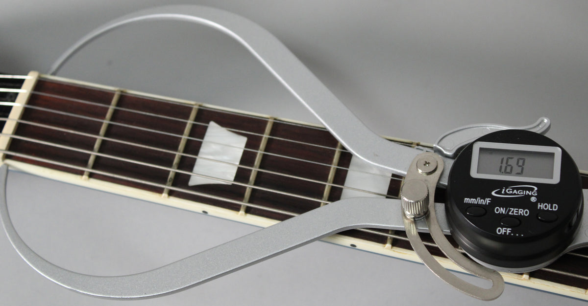 A digital string action gauge measures 1.69mm above the 12th fret of the guitar's dark rosewood fretboard with trapezoid inlays.