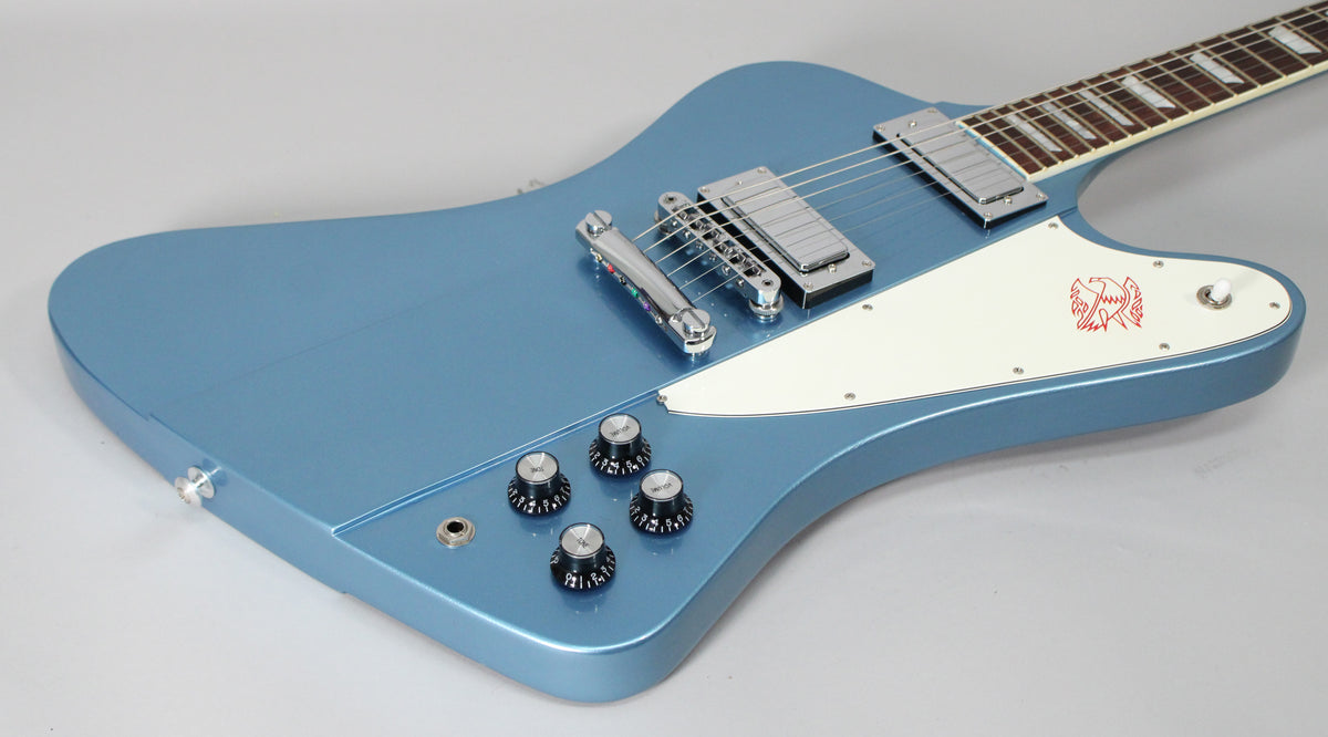 The Pelham Blue guitar body, with a white pickguard featuring a red bird graphic, is angled from the lower left, showing chrome hardware.