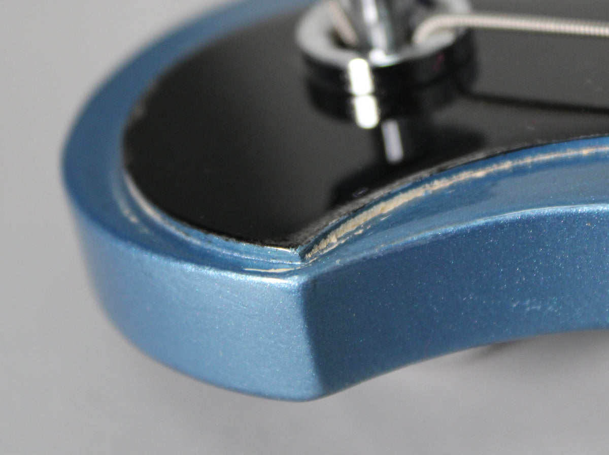 Close-up of the Pelham Blue headstock edge, showing paint chips and wear along the black truss rod cover.