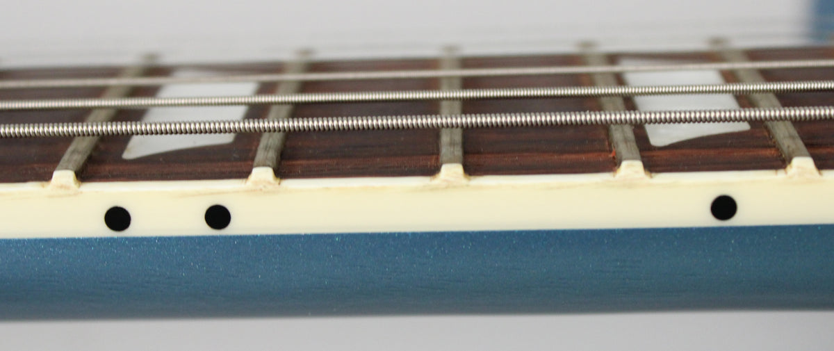Close-up of the Pelham Blue guitar's fretboard, showing dark wood, trapezoid inlays, side dots, and light binding with some grime.