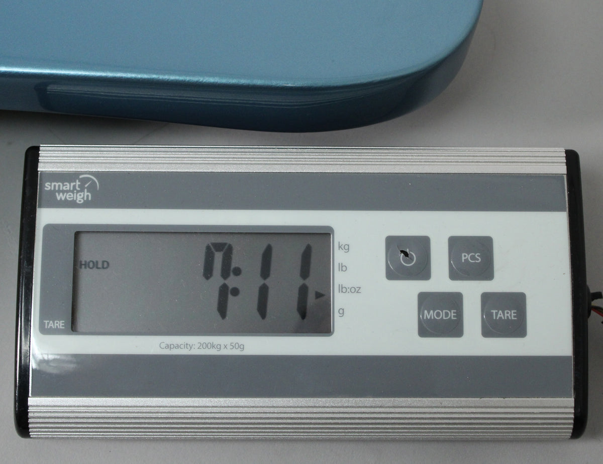 A close-up of a digital scale displaying "7:11 lb:oz" with a Pelham Blue guitar body resting on it.