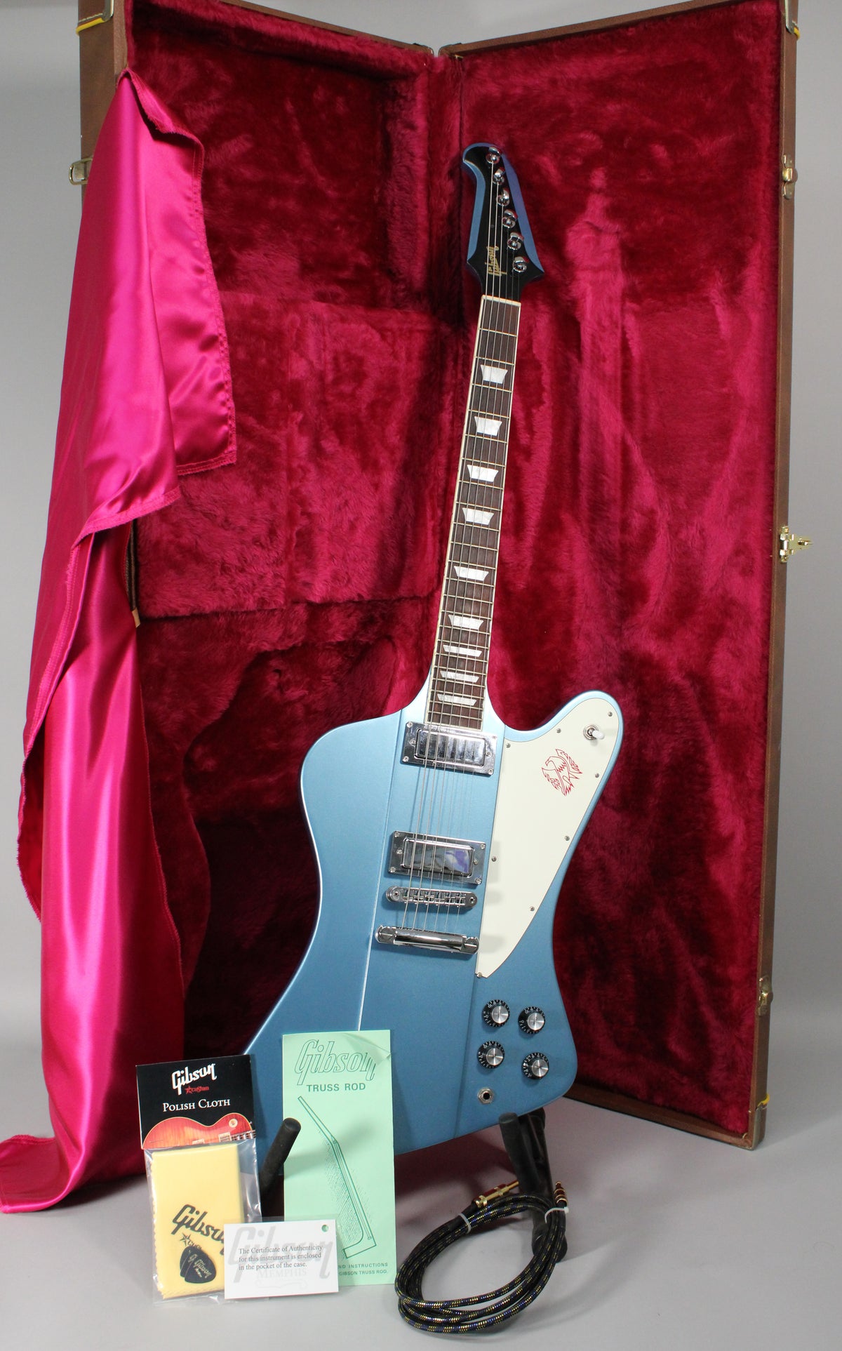 Pelham Blue Firebird T electric guitar with a white pickguard, chrome hardware, and four black control knobs, standing in its open case.