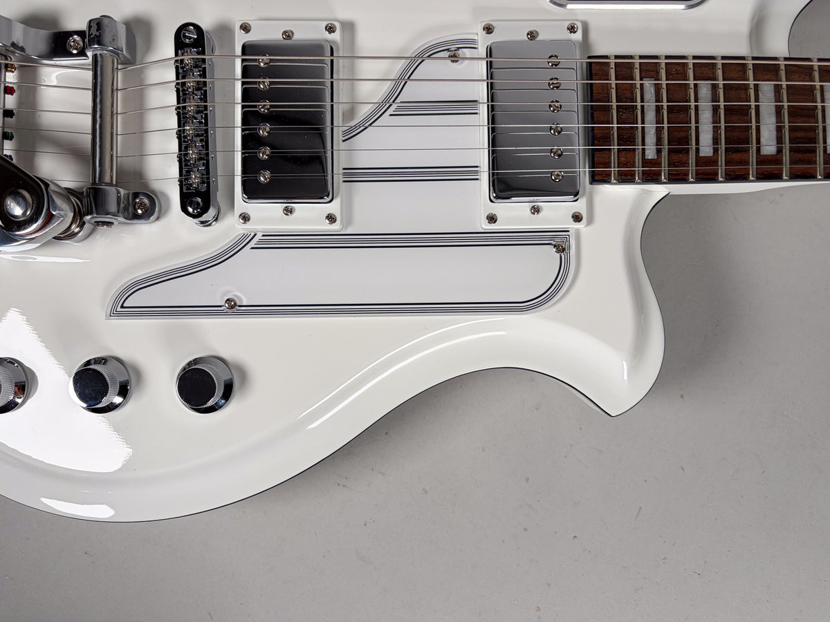 Close-up of the white guitar body, showing two chrome humbuckers, a Bigsby tremolo, tune-o-matic bridge, and three chrome control knobs.