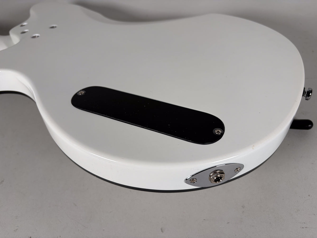 The guitar's white body, seen from the back, shows a black control cavity cover and a chrome output jack on the lower bout.
