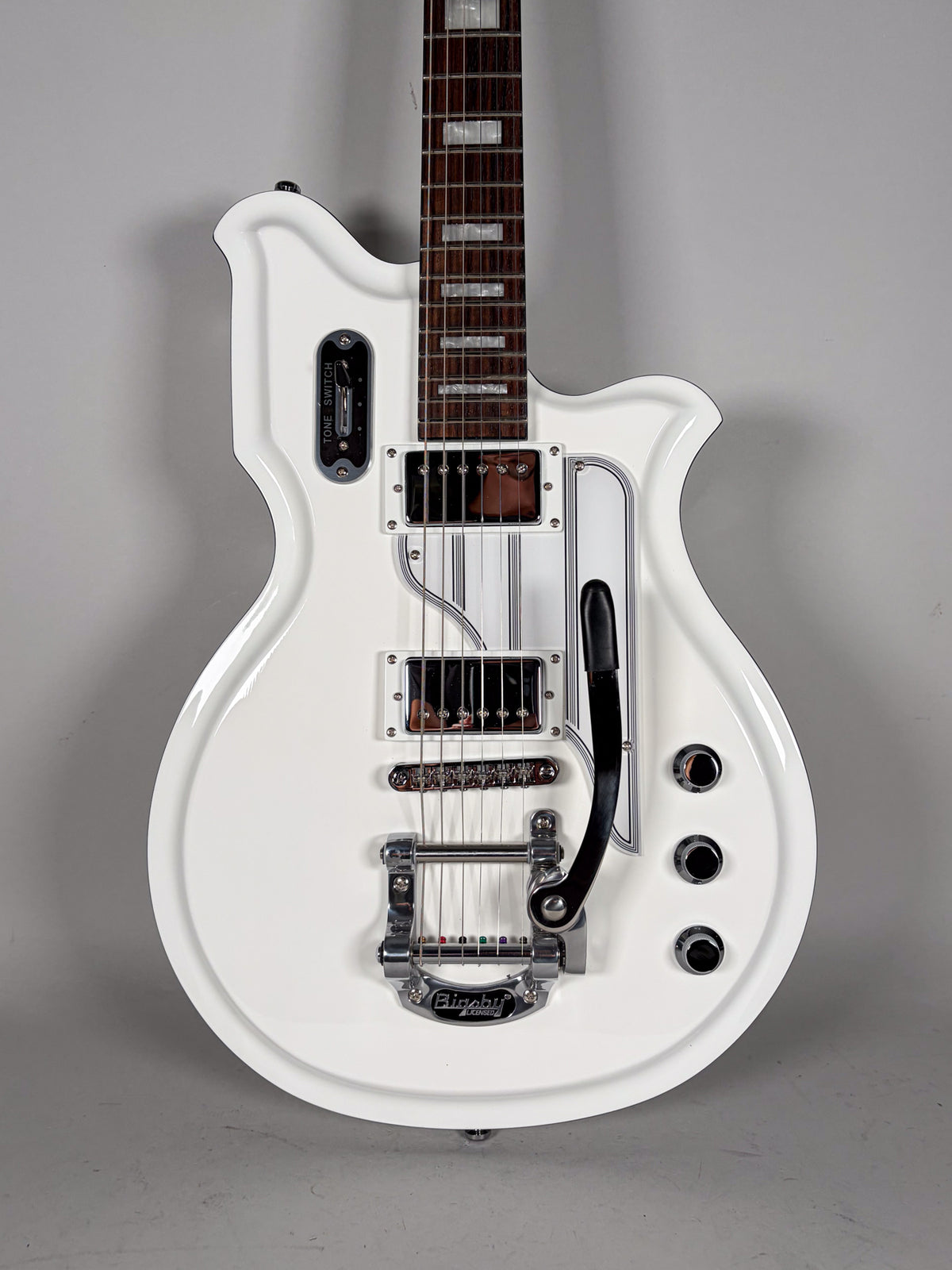 The white guitar body is centered, showing two humbuckers, a Bigsby tremolo, three control knobs, and a tone switch.