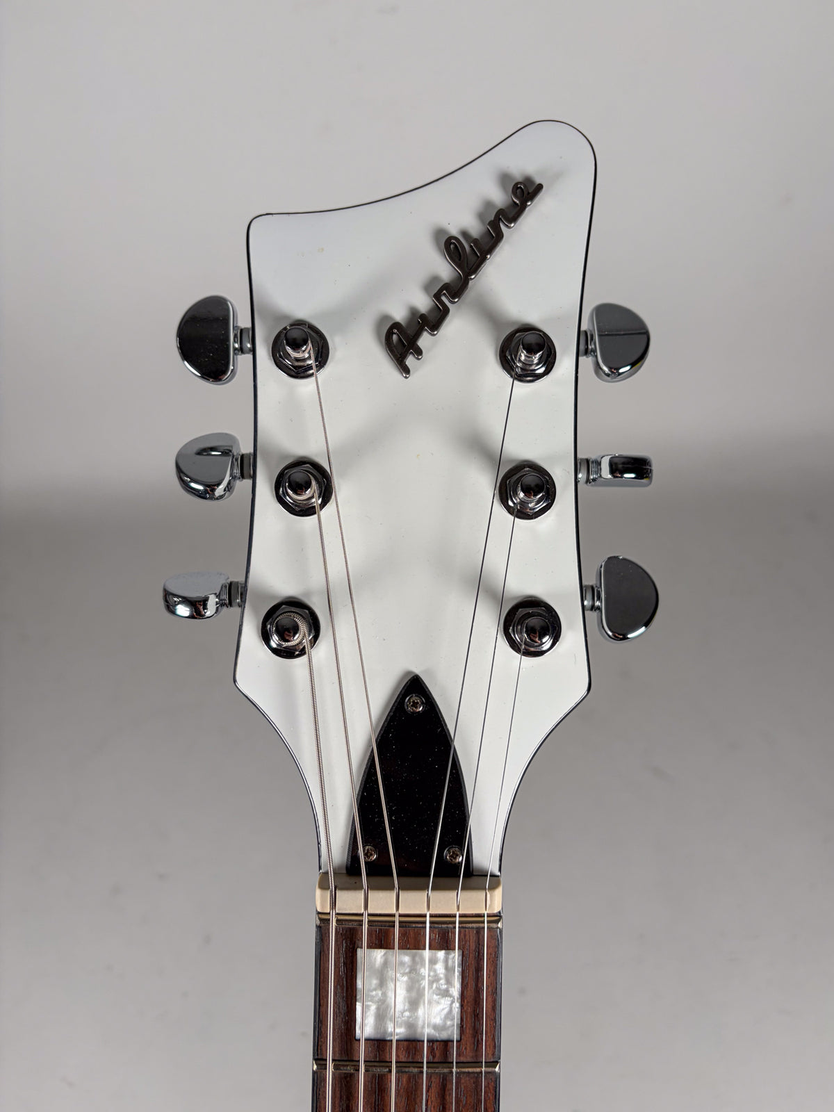 The white headstock of the guitar, with six chrome tuners and a dark brown fretboard with rectangular mother-of-pearl inlays.