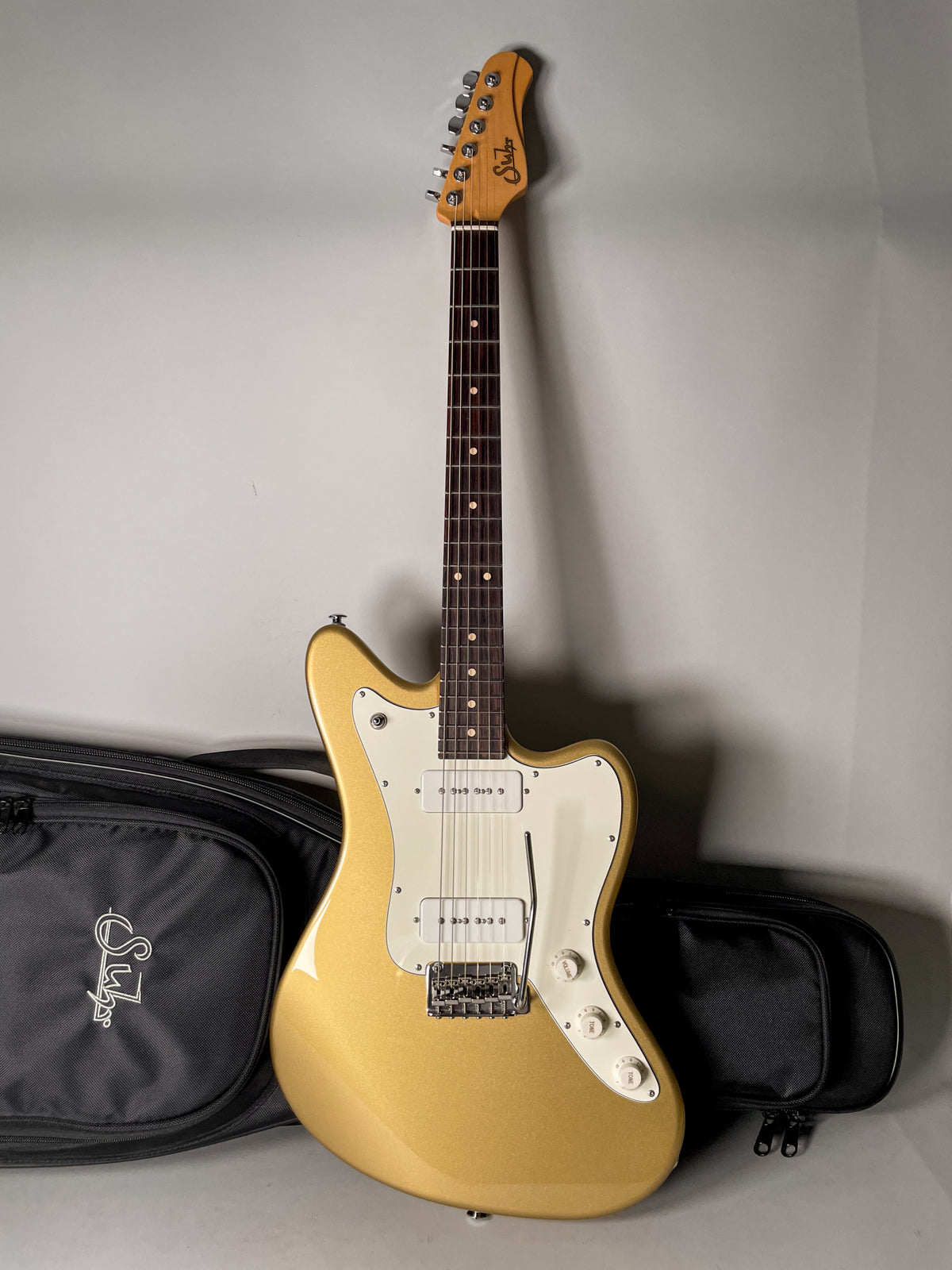 Full-length view of a gold sparkle offset-body electric guitar with a cream pickguard, two white P90 pickups, and a tremolo bar.