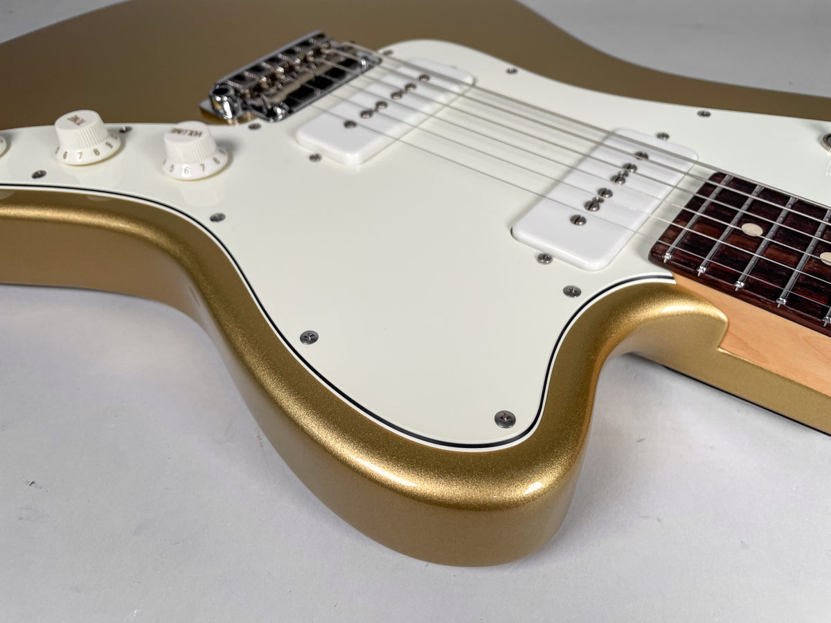 Close-up of a gold sparkle guitar body with a white pickguard, two white P90 pickups, and two white control knobs.