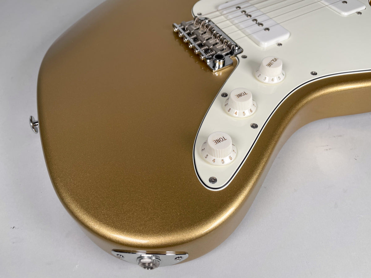 Close-up of a gold sparkle guitar body with white pickguard, three white control knobs, chrome bridge, and input jack.
