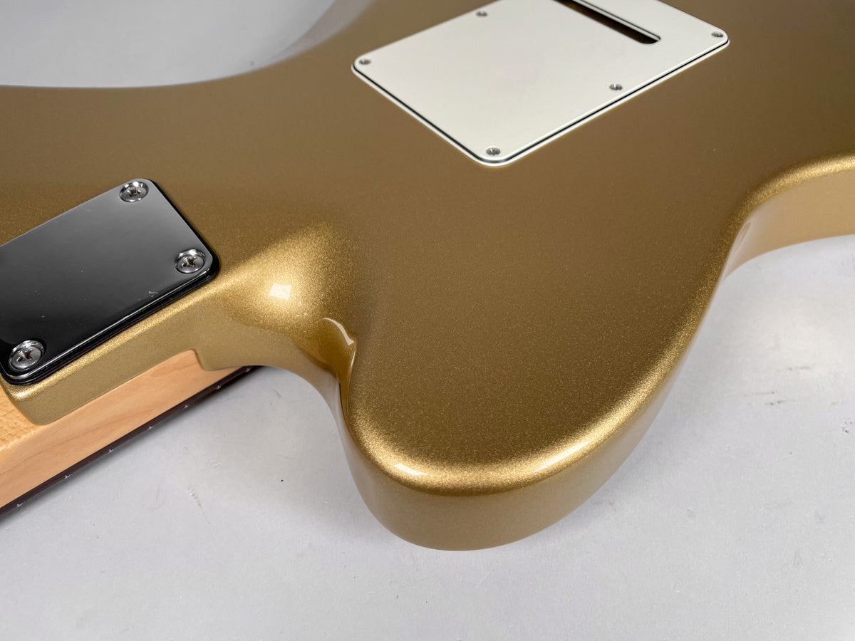 The back of a gold metallic guitar body, showing the neck plate, neck heel, and tremolo cavity cover.