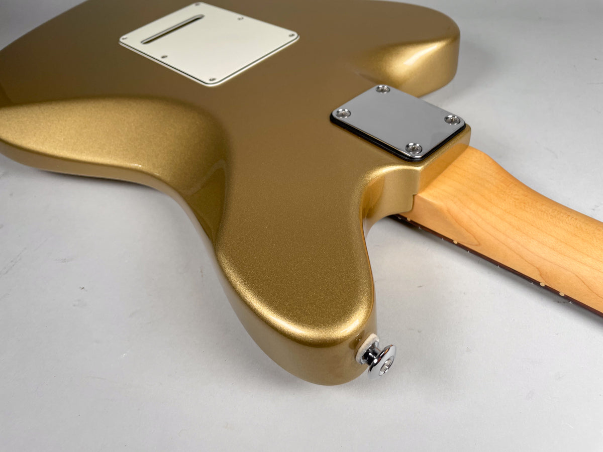 The back of a gold sparkle guitar body, showing the neck joint, output jack, and a white tremolo cavity cover.