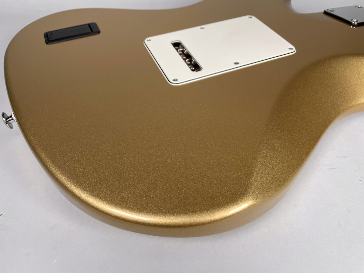 The back of a gold sparkle guitar body, showing a white tremolo cover and a black rectangular battery compartment.
