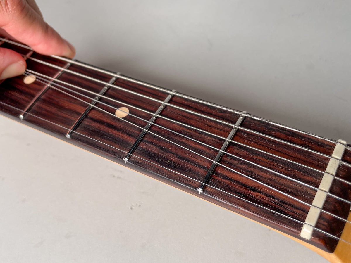 Close-up of a dark rosewood fretboard with light dot inlays, silver frets, and a bone nut, with a hand pressing strings.
