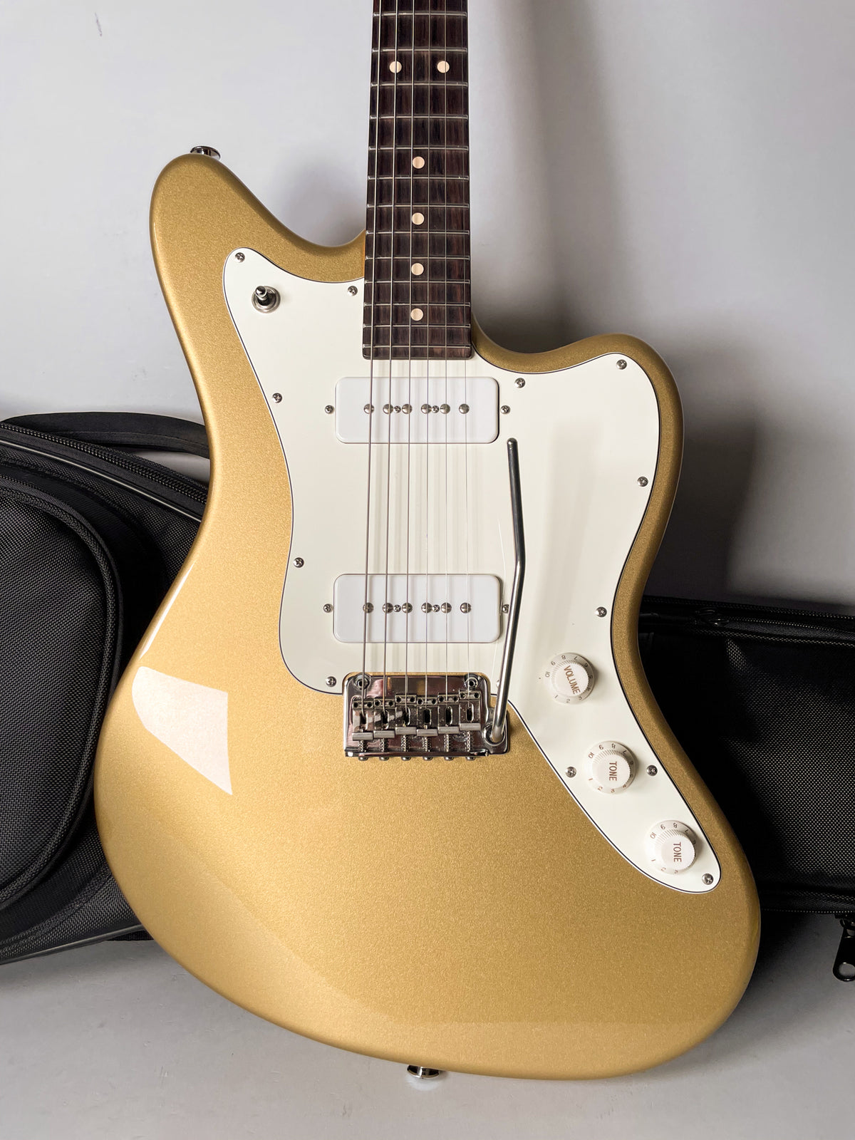 Gold sparkle finish electric guitar, angled from above, showing the body, white pickguard, two white P90 pickups, and three white control knobs.