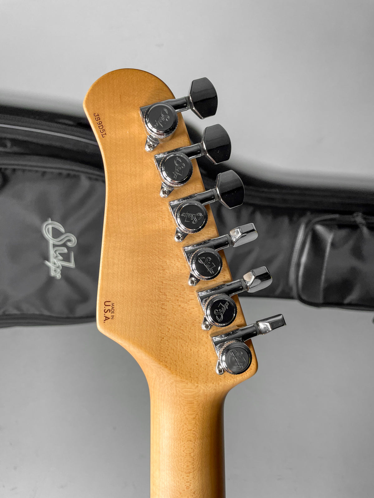 The guitar's maple headstock, viewed from the back, features six chrome tuners with black buttons, showing no visible wear.