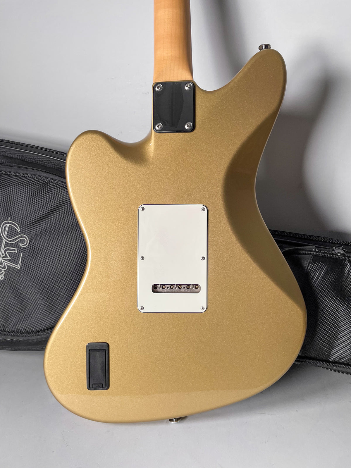 The back of a gold sparkle guitar with a natural maple neck, white tremolo cover, and black battery compartment.