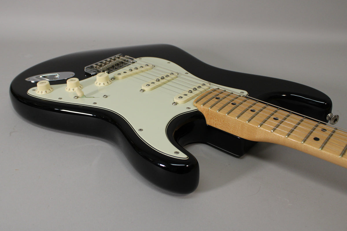 Black Stratocaster body with a white pickguard, three cream single-coil pickups, and a maple neck, viewed from the upper bout.