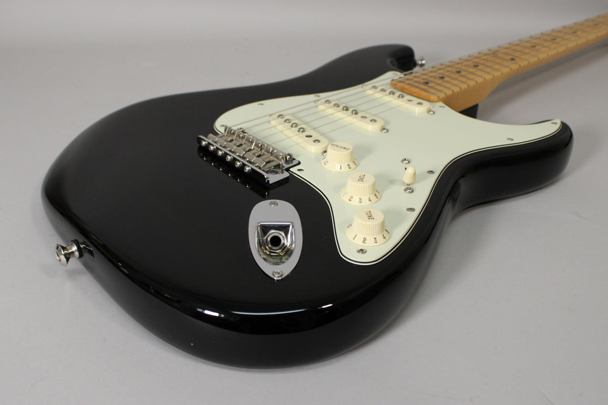 The glossy black Stratocaster body is angled from the lower left, showing the white pickguard, three cream single-coil pickups, and controls.