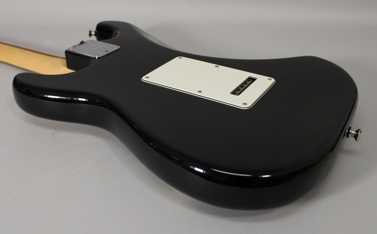 The glossy black guitar body is angled, revealing the light cream tremolo cover and a chrome neck plate.