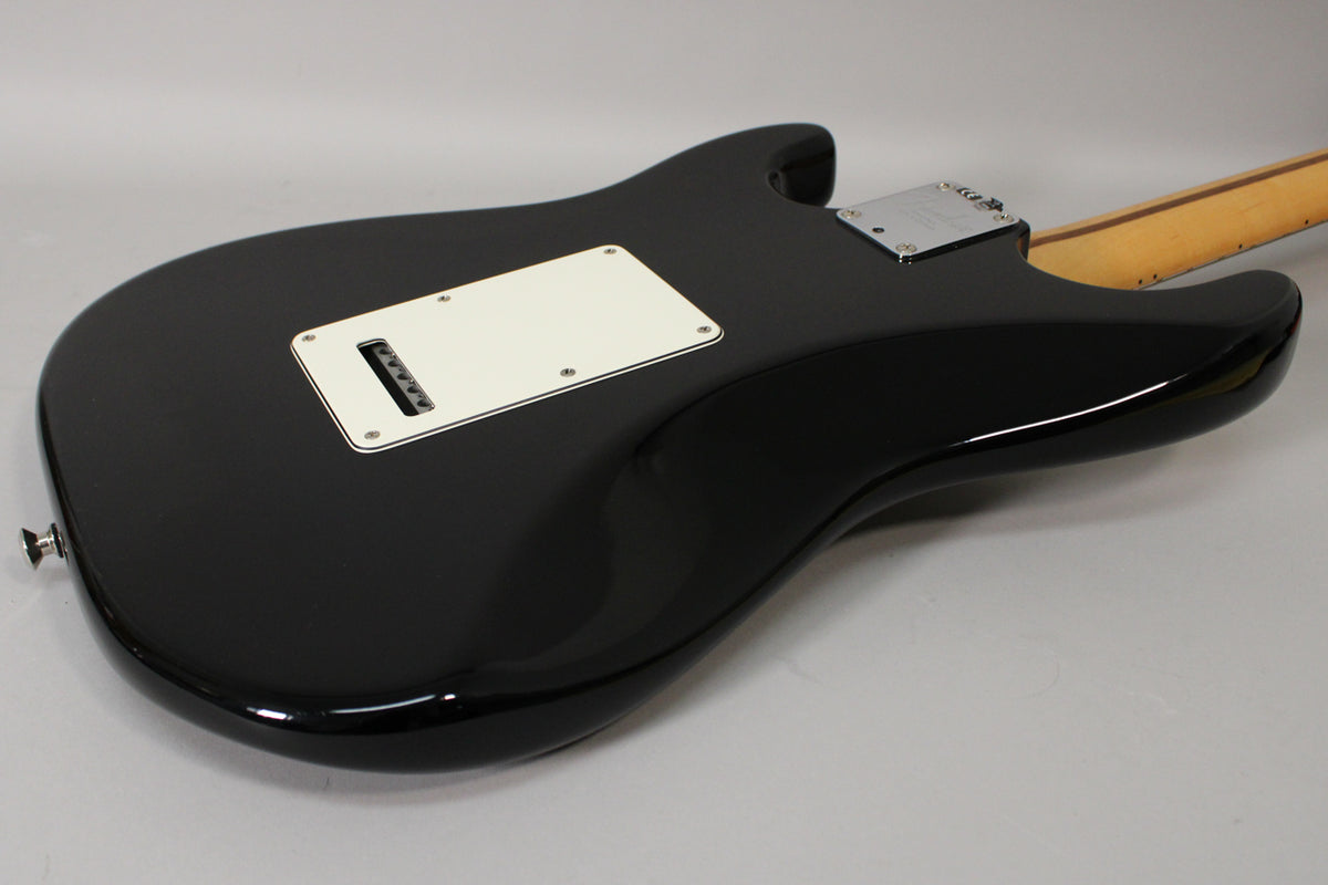 The black Stratocaster's glossy back shows a white tremolo cavity cover, chrome neck plate, and a light maple neck.