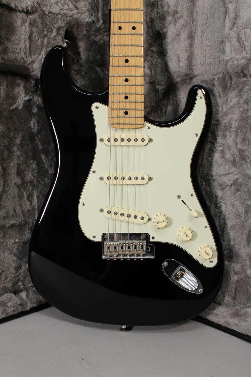 Full-frame view of a glossy black Stratocaster with a maple fretboard, cream pickguard, three single-coil pickups, and chrome hardware.