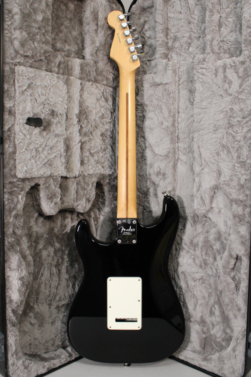 The black Stratocaster's back is visible, showing a maple neck, chrome tuners, and a white tremolo cover, in its plush grey case.