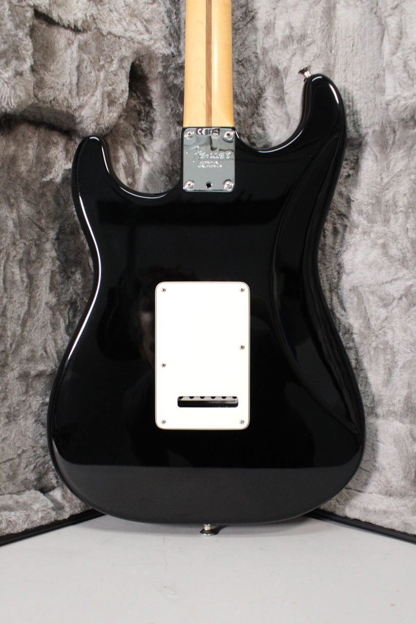 The back of a glossy black Stratocaster body with a white tremolo cover, a chrome neck plate, and a light maple neck.