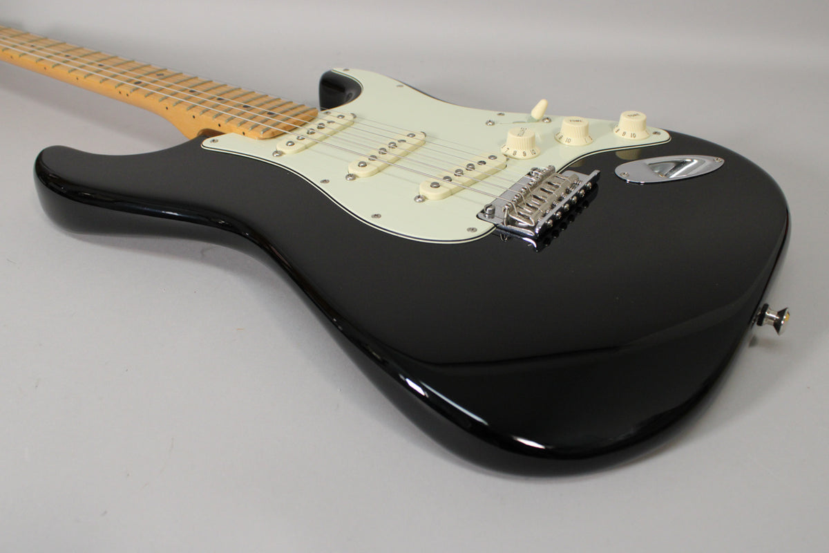 The black Stratocaster's glossy body and light maple neck are angled, revealing a white pickguard, three single-coil pickups, and chrome hardware.