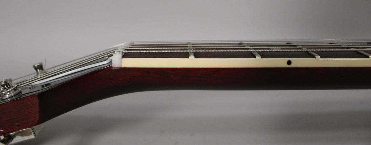 The guitar's dark cherry neck and headstock are viewed from the side, showing the white nut, frets, and tuning pegs.