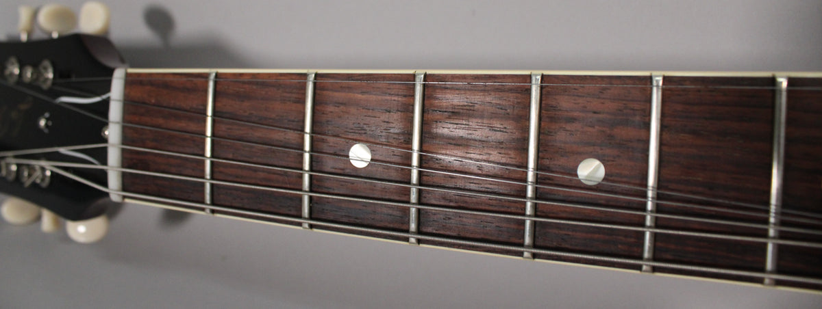 Close-up of the dark rosewood fretboard with white binding, showing five frets, dot inlays, and the white nut and headstock edge.