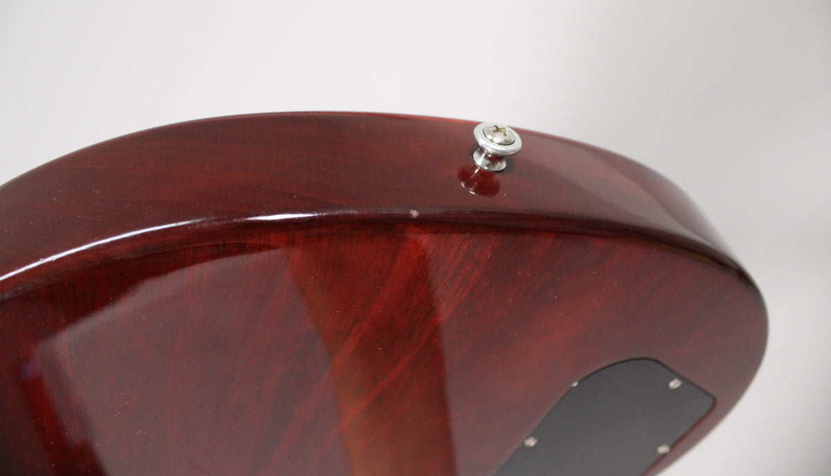 Close-up of the guitar's dark cherry body, showing a small ding near the strap button and the black control cavity cover.