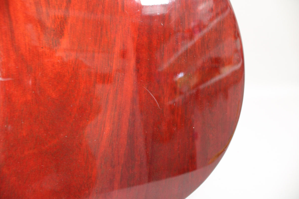 Close-up of the dark cherry red guitar body, showing a visible scratch on the glossy finish and wood grain beneath.