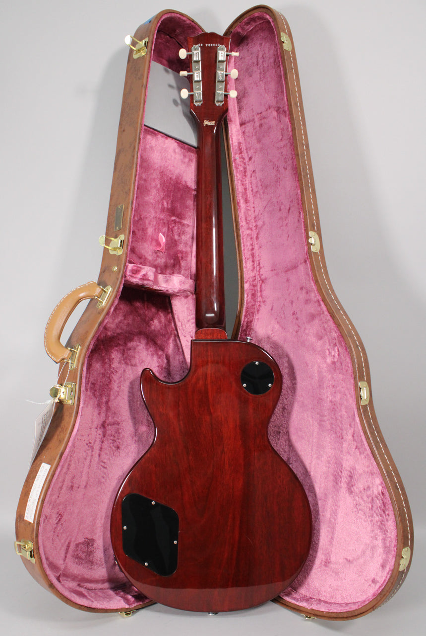 The guitar's dark cherry back and neck are visible, with two black control plates, resting in a brown case with pink plush lining.