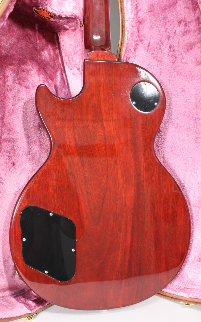 The guitar's dark cherry back, with visible wood grain, features two black control cavity covers and a glossy finish, resting in a pink velvet case.
