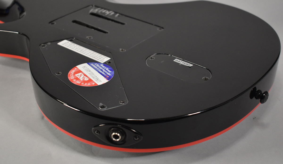 The guitar's glossy black back, with red binding, shows control cavity covers, a battery compartment, and the output jack.