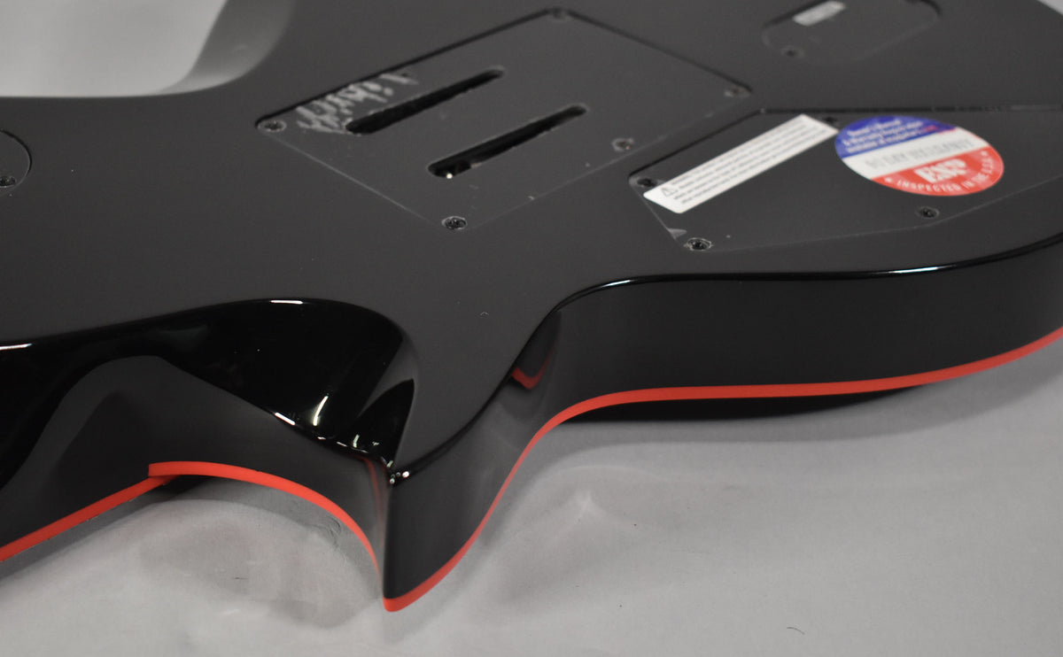 The guitar's glossy black body, with red binding, is viewed from the back, showing control cavity covers and a sticker.
