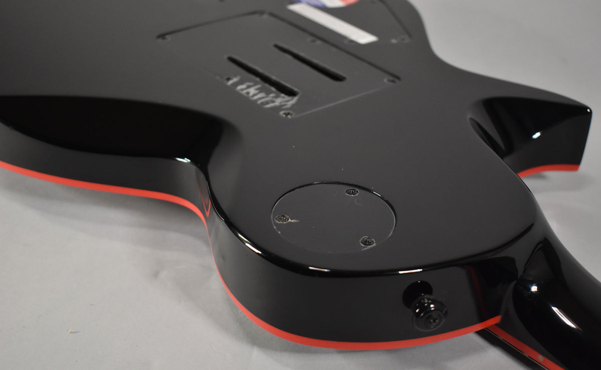 The back of a glossy black electric guitar with red binding, showing the control cavity and output jack.