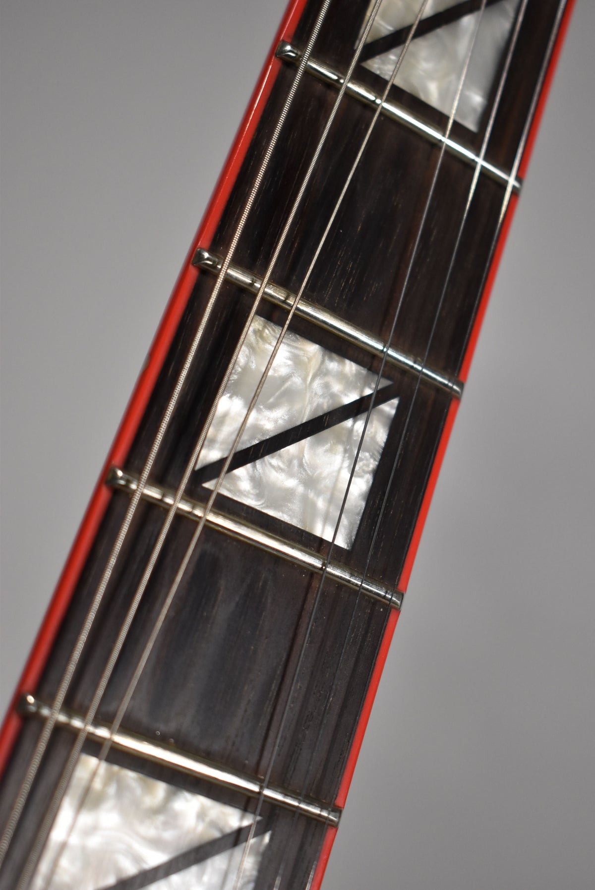 Close-up of the dark fretboard with white pearloid triangle inlays and a thin red binding along the edge.