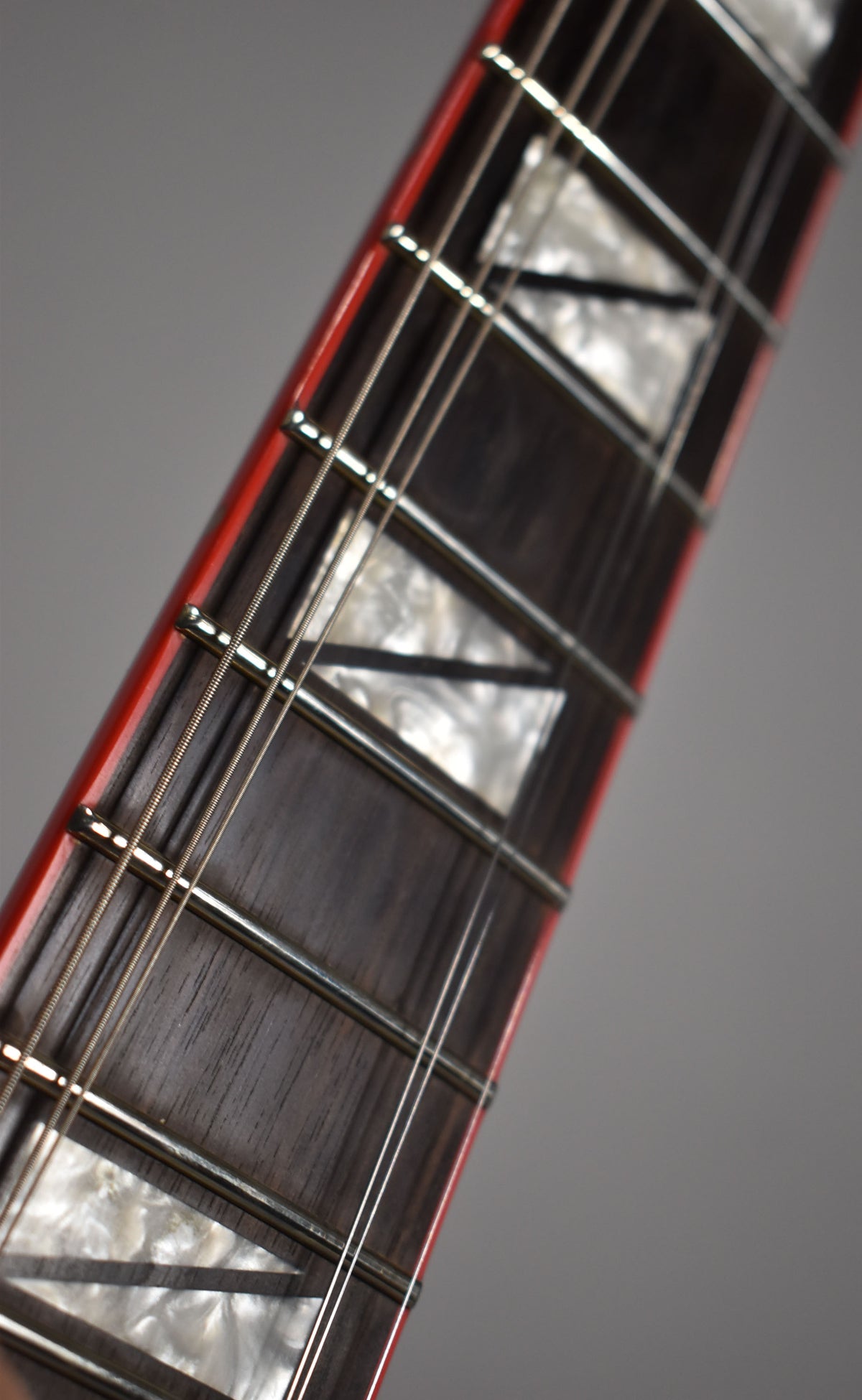 Close-up of the guitar's dark fretboard with mother-of-pearl triangle inlays, red binding, and silver frets and strings.